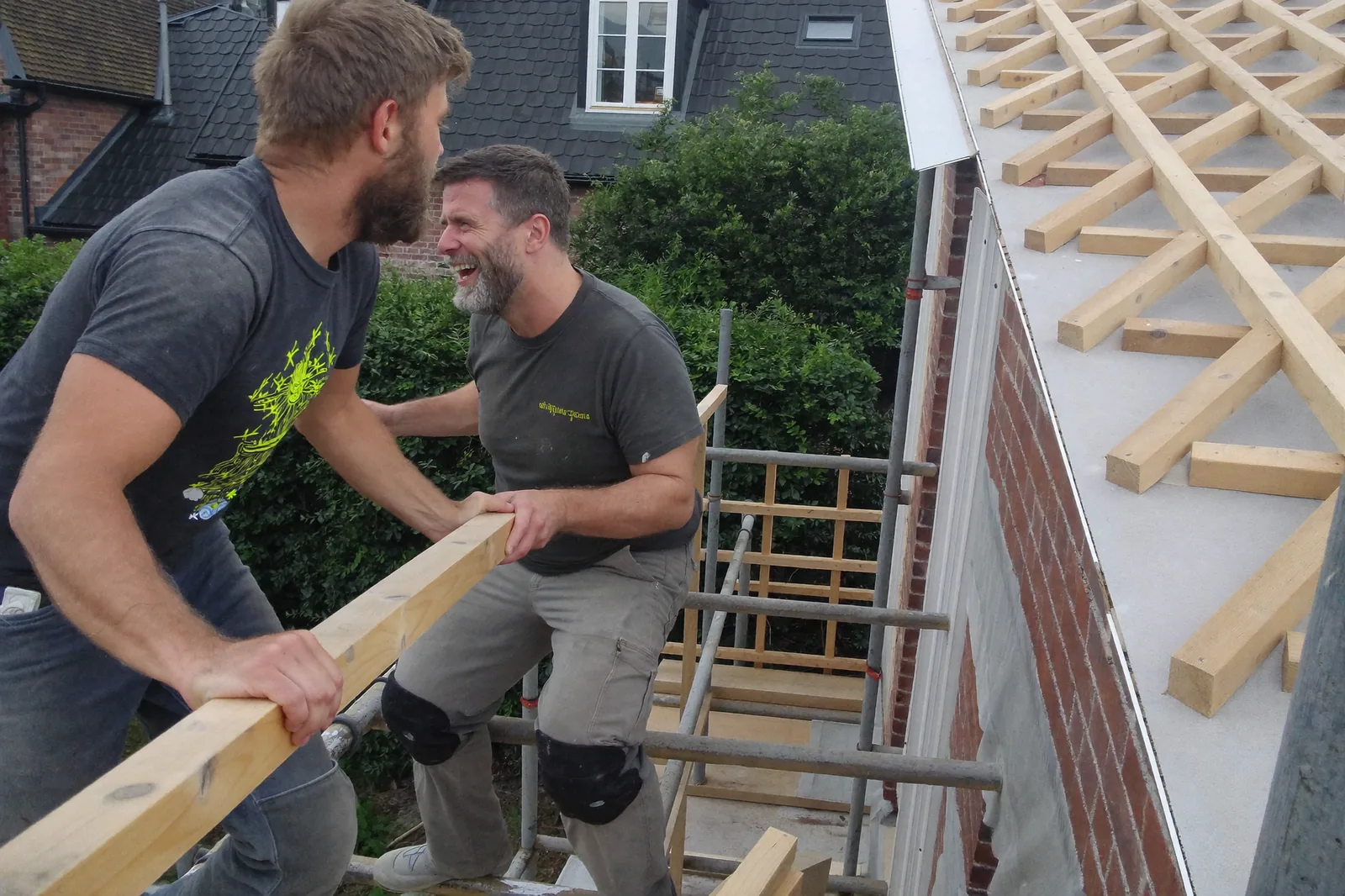 Deux couvreurs sur un échafaudage se passent une latte, lattage neuf en arrière-plan